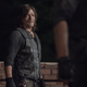 Daryl, in a black leather vest and long-sleeved shirt, stands in front of a low brick wall at night.